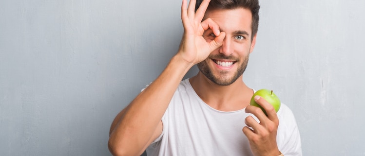 Man holding an apple making a circle with his hands around his eye, eye exam Springfield MA, comprehensive eye exam Western MA, eye doctor, Dr. John Papale